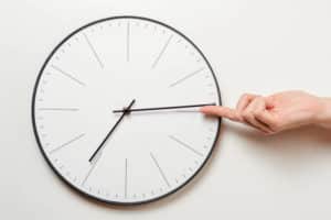 La main d’une femme arrête le temps sur une horloge ronde, un doigt féminin ramène l’aiguille des minutes en arrière, concept de gestion du temps et de respect des délais.