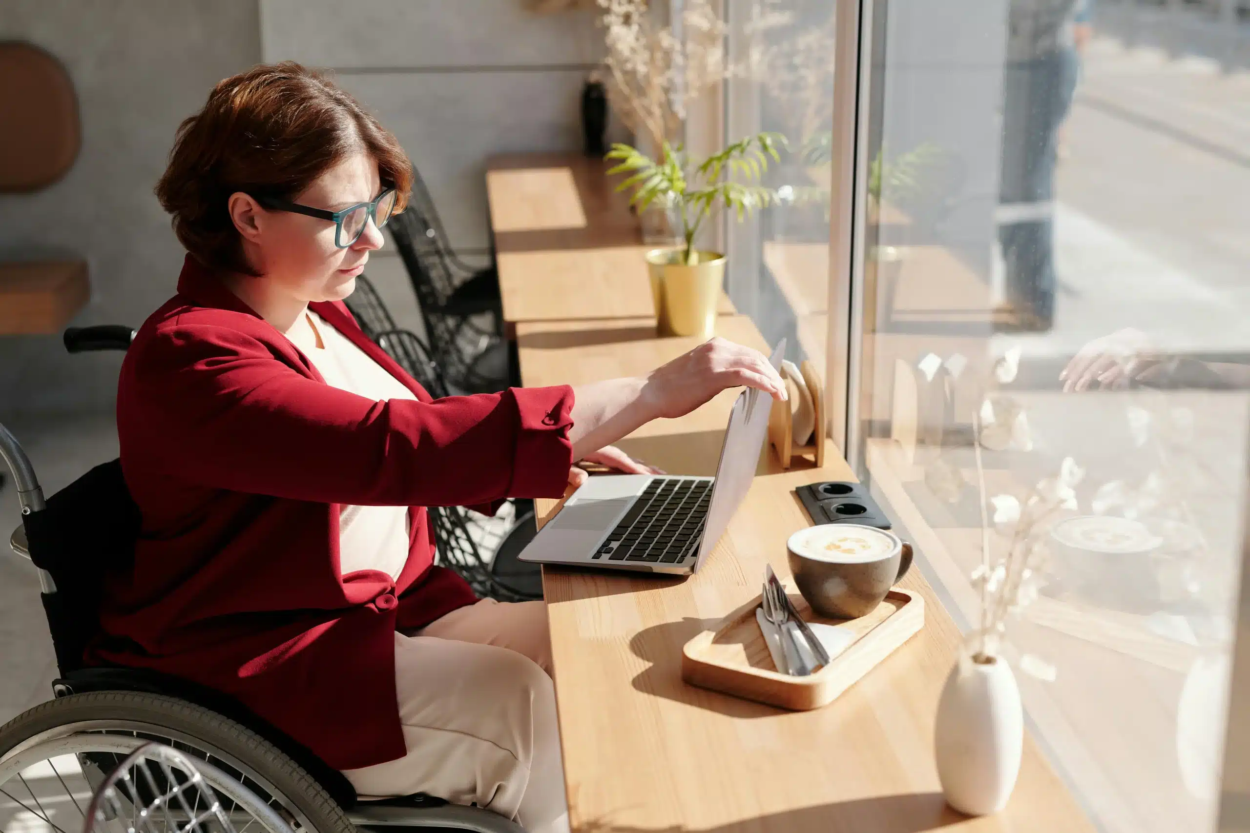 Femme en fauteuil roulant travaillant sur un ordinateur dans un café ensoleillé