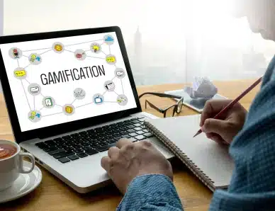 Ordinateur affichant le concept de gamification avec des icônes, utilisé par une personne prenant des notes.