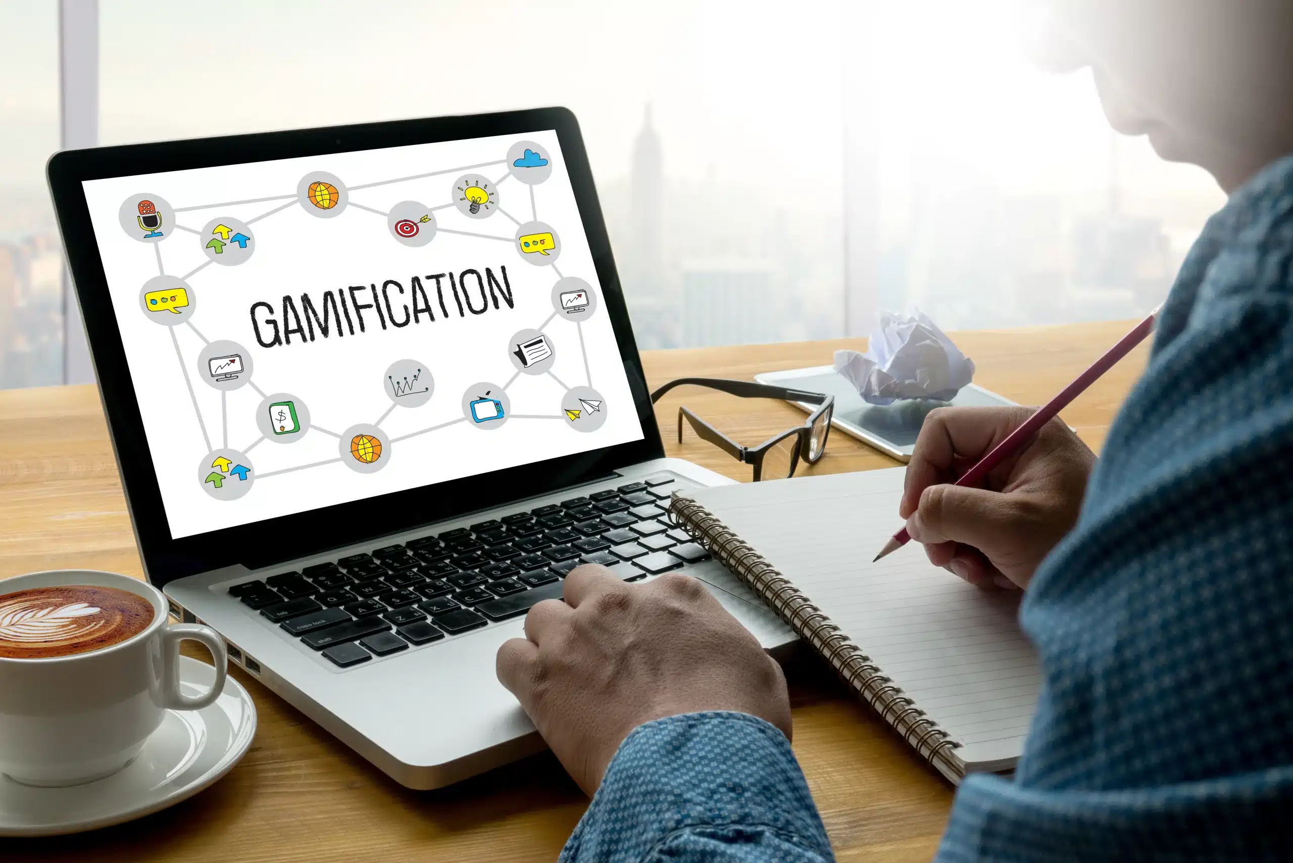 Ordinateur affichant le concept de gamification avec des icônes, utilisé par une personne prenant des notes.