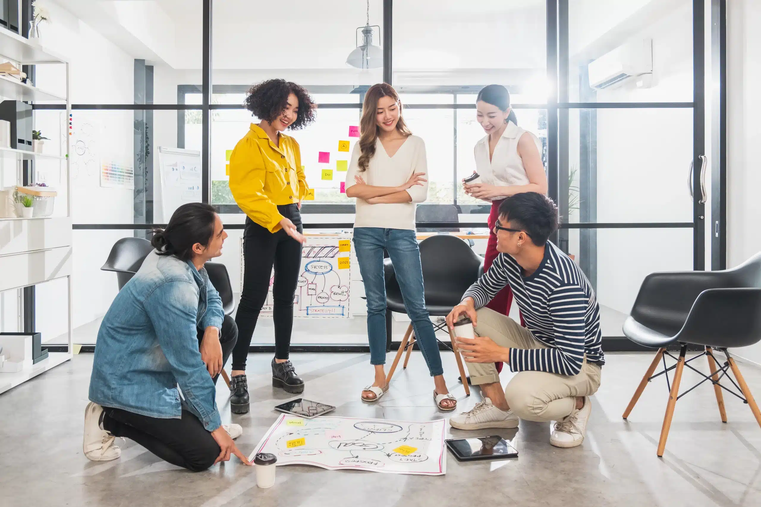 Groupe de jeunes adultes en workshop, discutant autour de plans au sol dans un espace de coworking lumineux