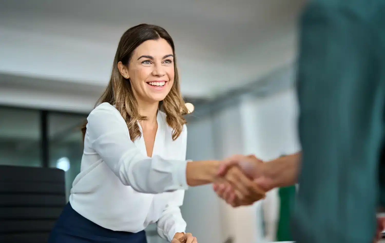 Femme souriante serrant la main d’un interlocuteur lors d’un entretien professionnel