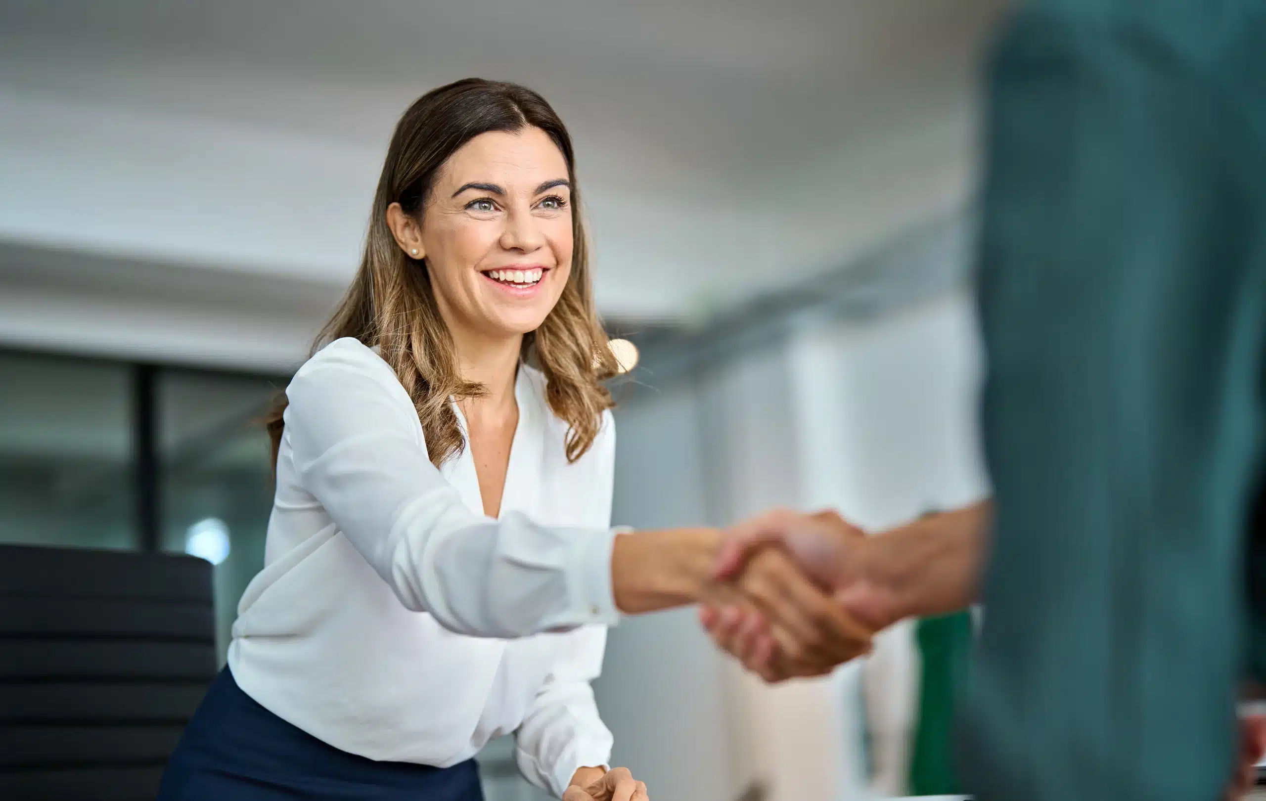 Femme souriante serrant la main d’un interlocuteur lors d’un entretien professionnel