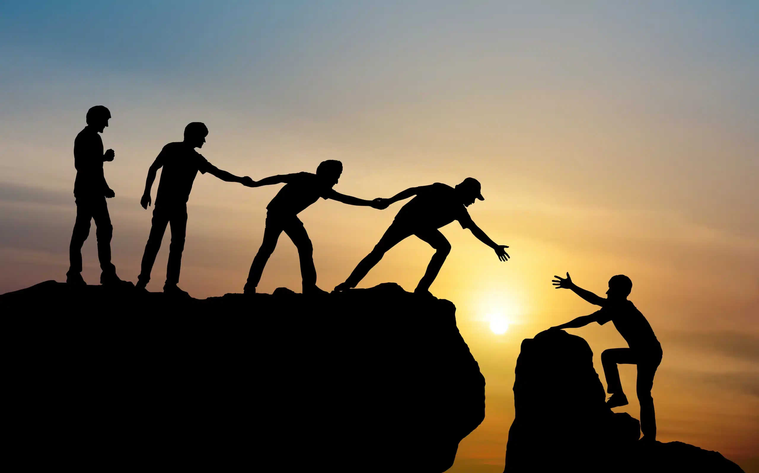 Silhouettes d’un groupe avec un leader aidant une personne à gravir un obstacle