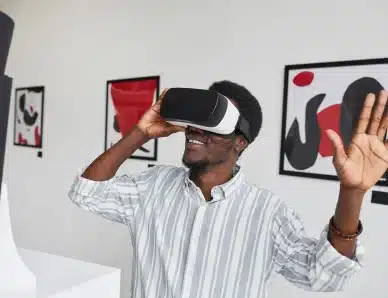 Homme souriant utilisant un casque de réalité virtuelle dans une galerie d'art contemporaine, levant la main avec enthousiasme
