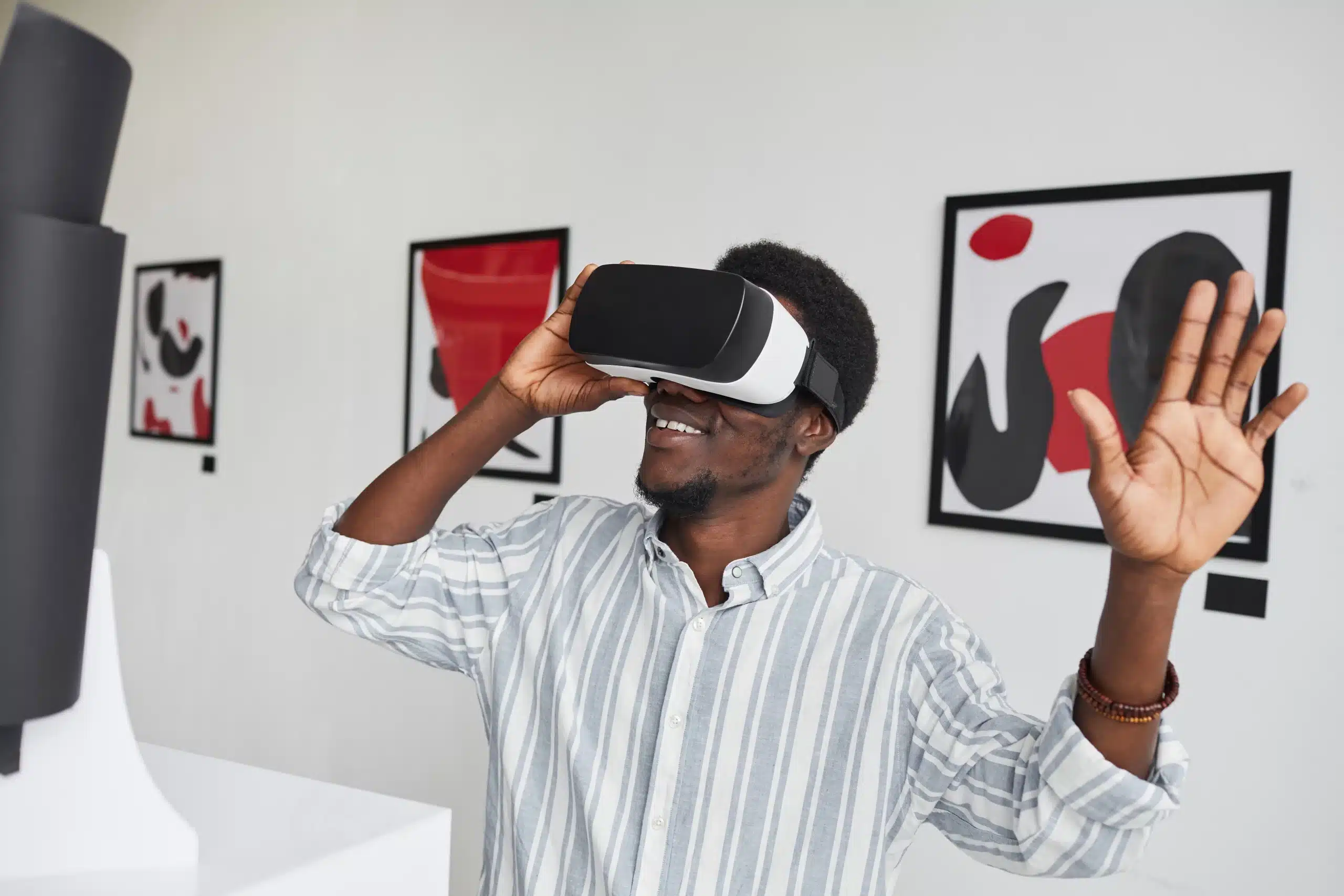 Homme souriant utilisant un casque de réalité virtuelle dans une galerie d'art contemporaine, levant la main avec enthousiasme