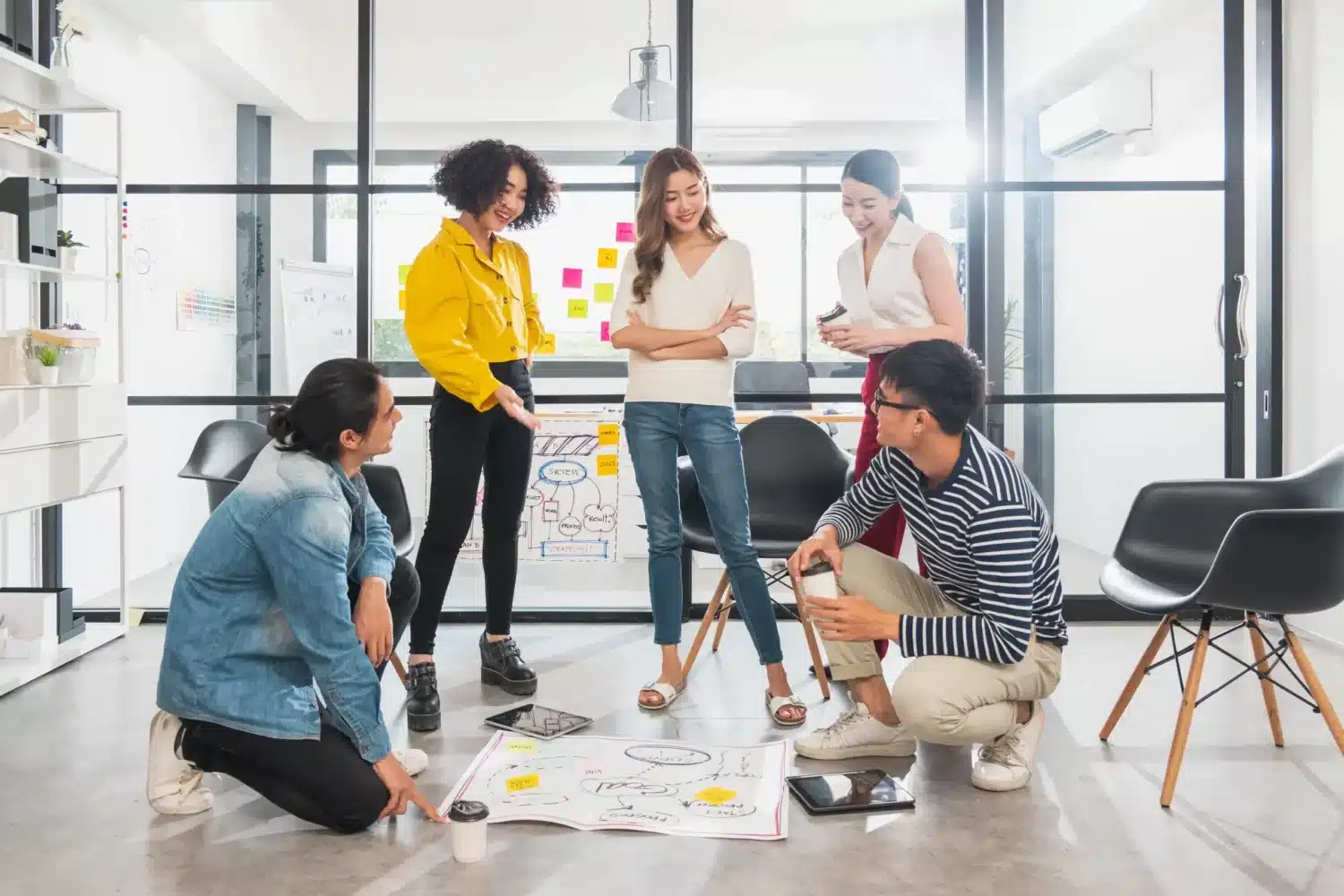 Groupe de jeunes adultes en workshop, discutant autour de plans au sol dans un espace de coworking lumineux