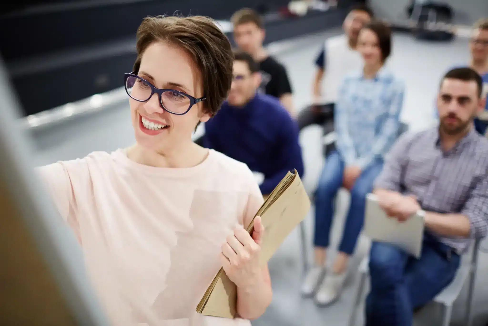 Formatrice écrivant sur un tableau et animant un atelier de management devant un groupe d'adultes attentifs