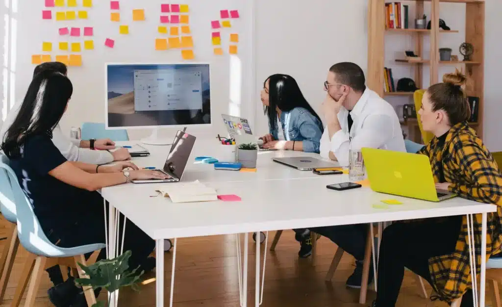 Groupe de personnes en réunion avec des ordinateurs portables et des post-it au mur