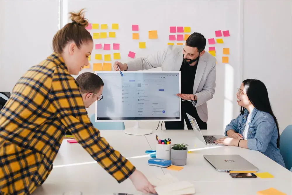 Équipe en réunion de travail collaboratif avec un écran et des post-it sur le mur
