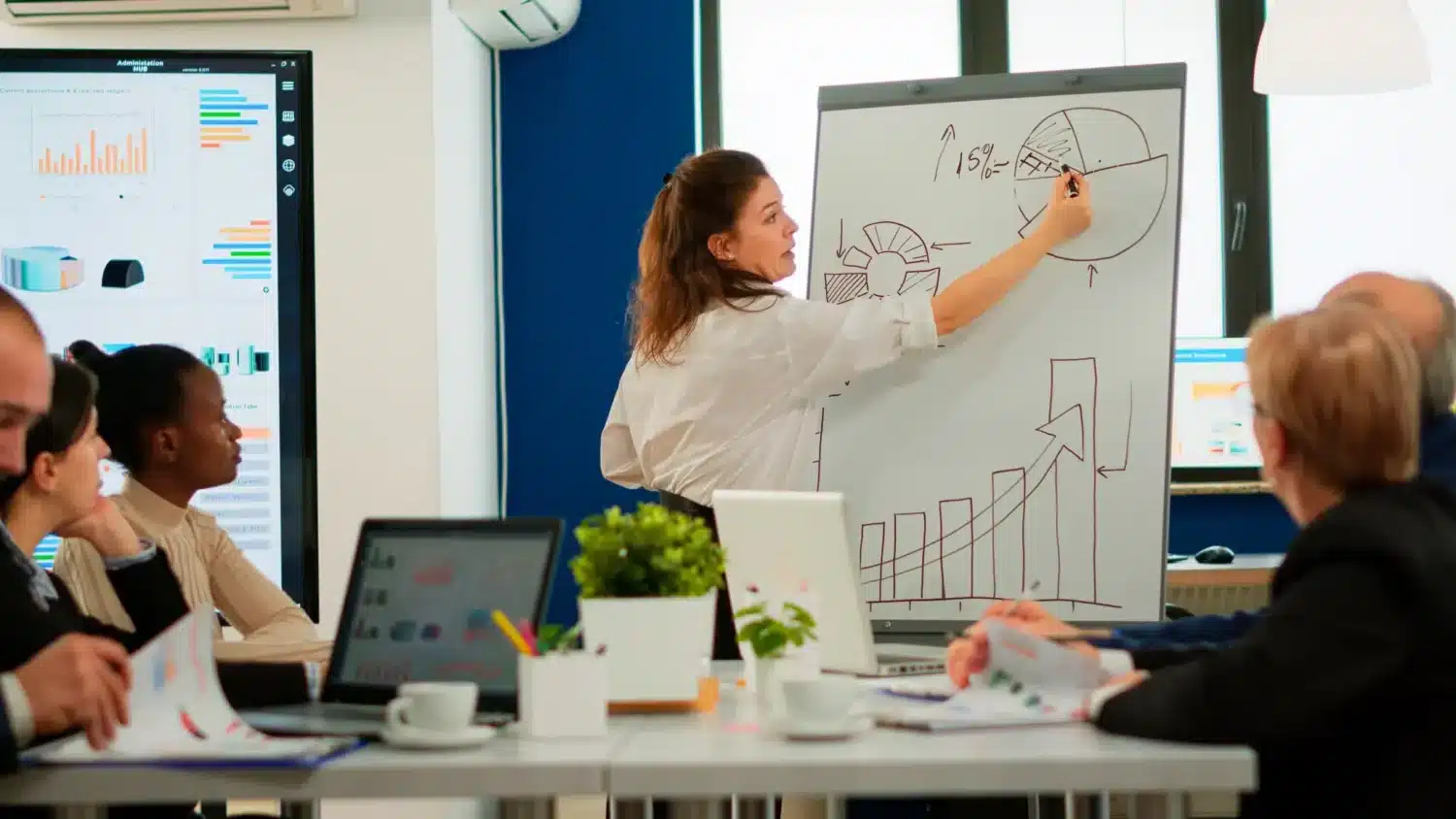 Femme présentant des graphiques sur un tableau blanc lors d'une réunion d'équipe en entreprise