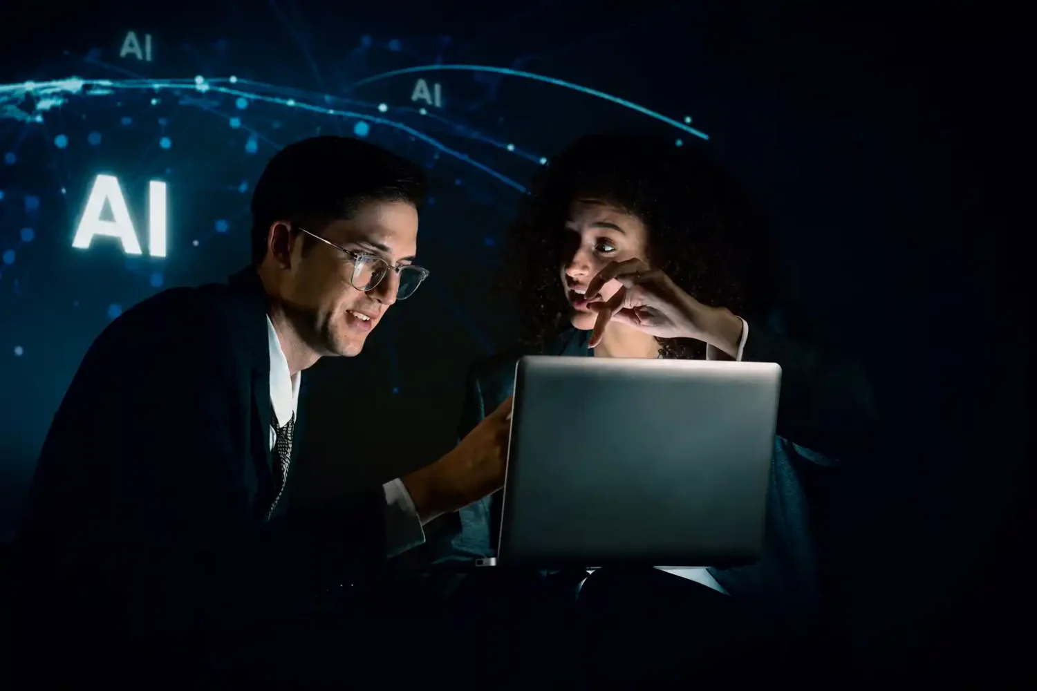 Deux professionnels collaborent devant un ordinateur portable dans une ambiance sombre et futuriste, avec des éléments visuels bleus liés à l’intelligence artificielle en arrière-plan.